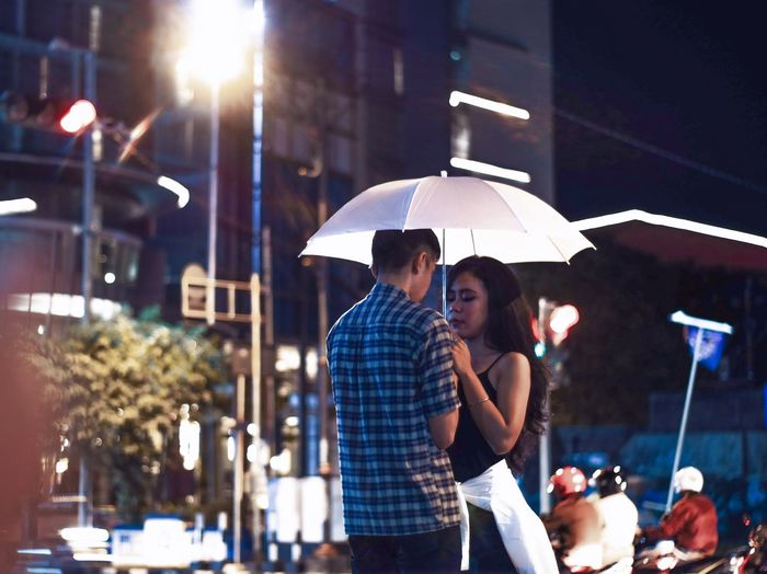 Young couple under umbrella standing in city