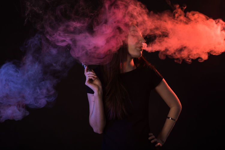Close-up of woman with smoke against black background