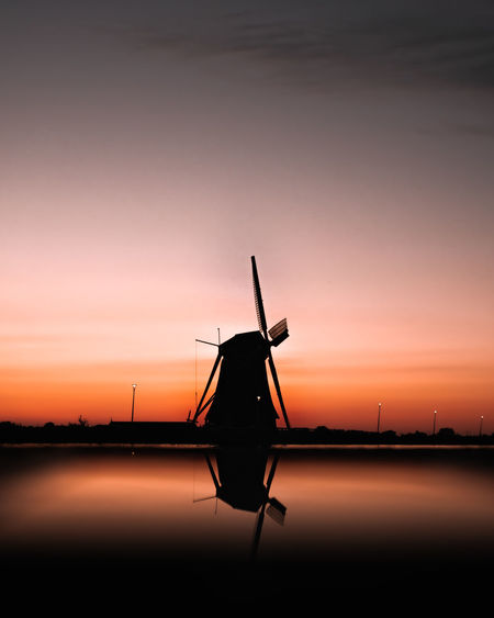 Silhouette of a mill against sky during sunset