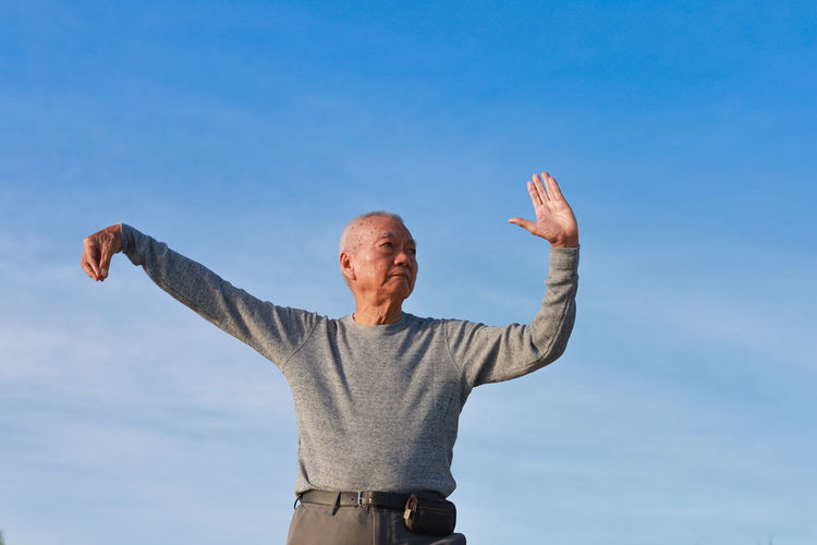 Low angle view of senior man exercising against blue sky