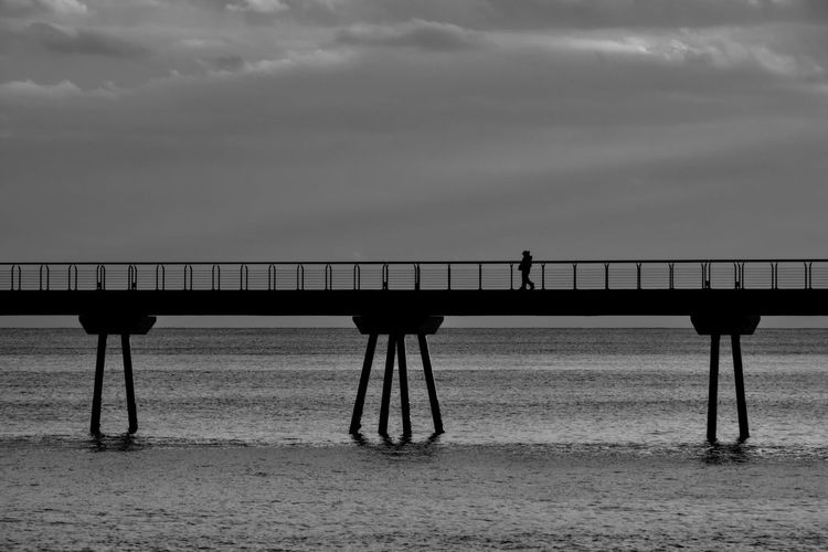 Silhouette people standing on bridge over sea against sky