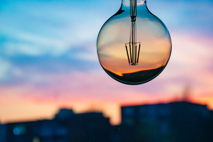 Close-up of glass hanging against sky during sunset