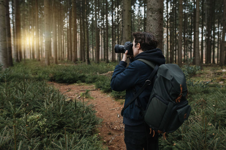 Rear view of man photographing in forest