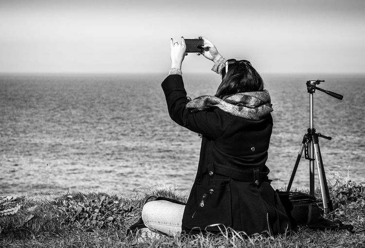 Rear view of woman photographing sea through smart phone
