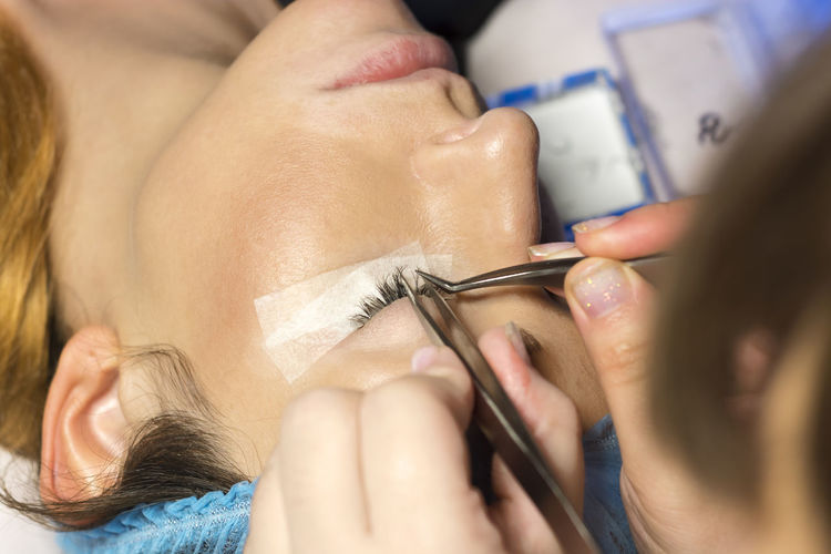 Beautician with applying false eyelash to customer