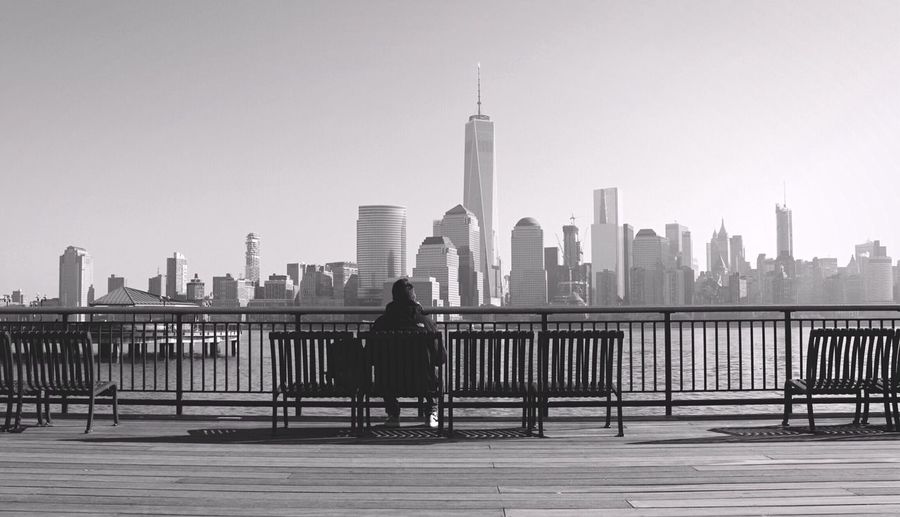 Rear view of man sitting on bench against one world trade center in city
