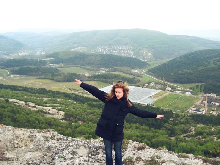 Beautiful woman standing with arms outstretched against valley and mountains