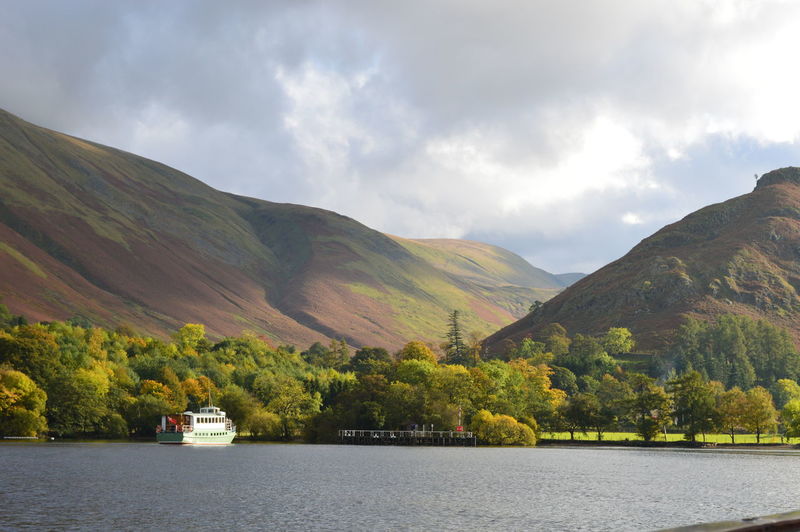 Ferry sailing in river by mountains against cloudy sky