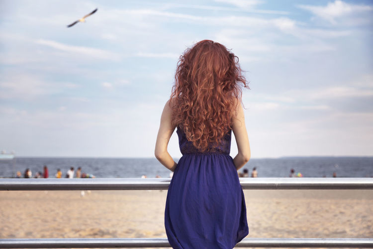 Rear view of young woman standing by railing against sky