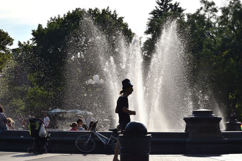 Side view of man walking on footpath by fountain during sunny day