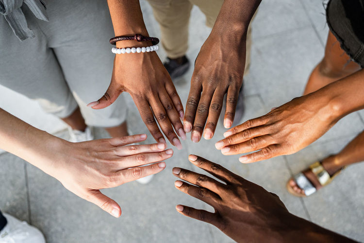 High angle of crop unrecognizable multiracial company of friends stacking hands together on street on sunny day