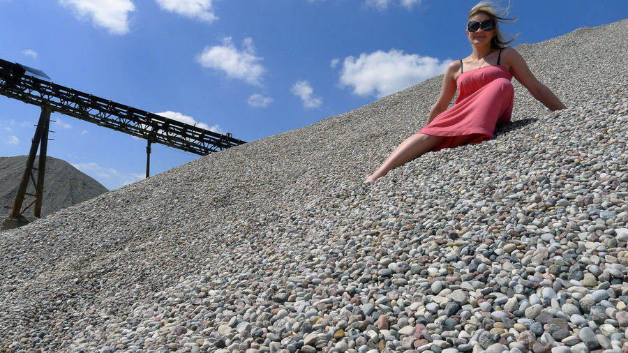 Low angle view of woman sitting on gravel against sky