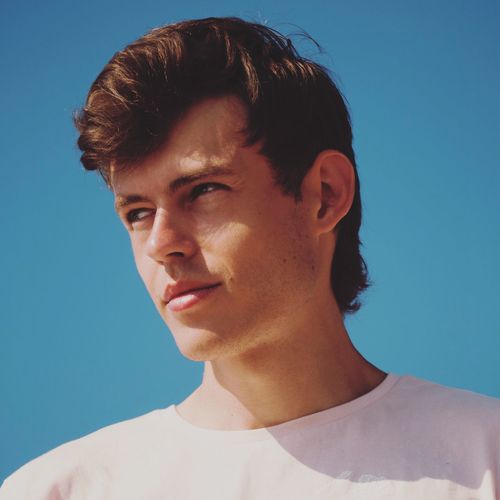 Close-up of young man looking away against blue sky