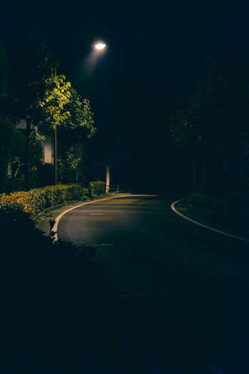 Empty road amidst trees against sky at night