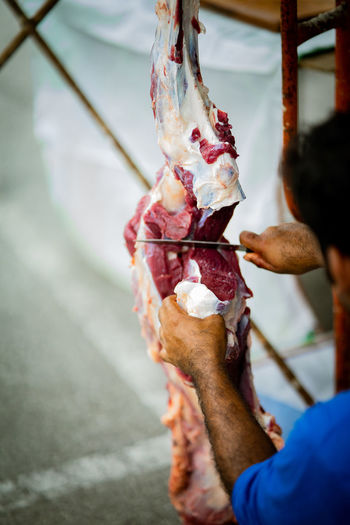 A man with a knife is cuttting the meat hanging on the hook.