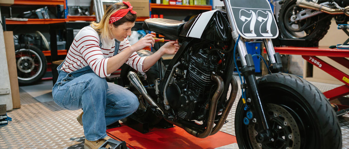 Mechanic woman repairing custom motorcycle on factory