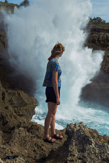 Full length side view of woman standing by splashing water on rock