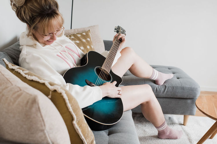 Woman sat playing guitar at home on the couch