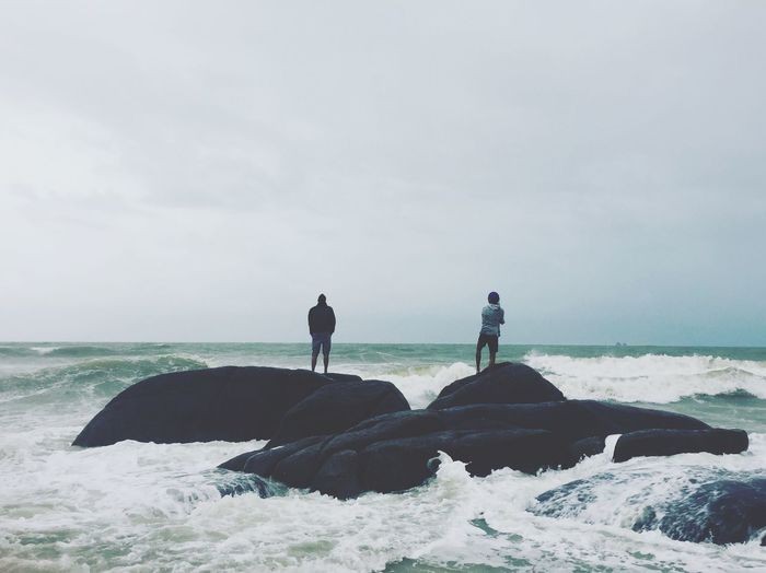 Friends standing on rock against sea at beach