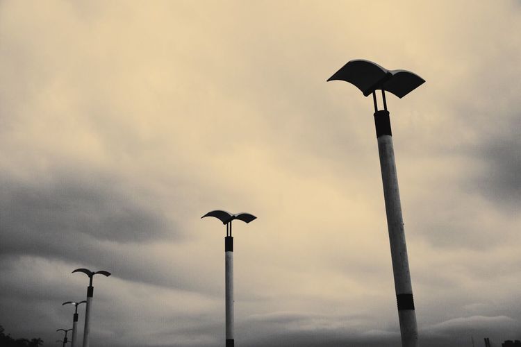 Low angle view of silhouette bird perching on street light against sky