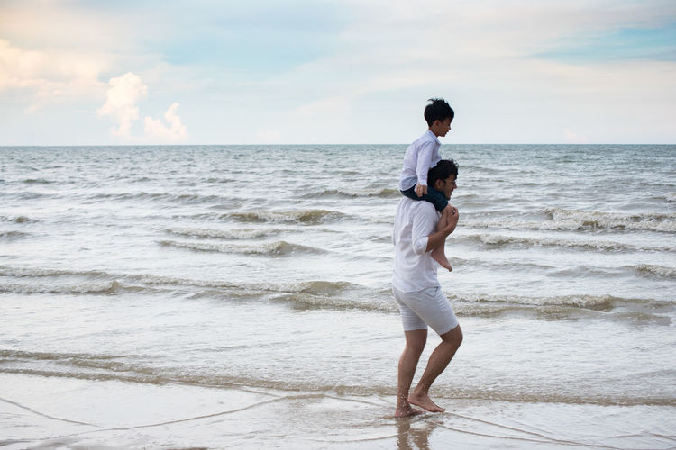 Man carrying boy on shoulder while walking at beach