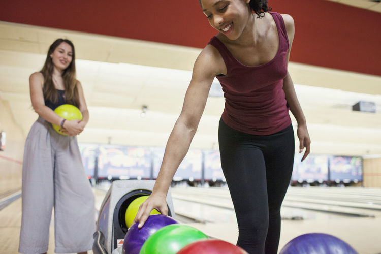 A young woman picking up a bowling ball.