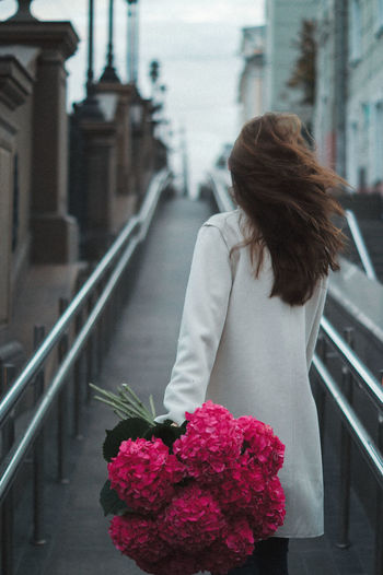 Rear view of woman with pink flowers walking in alley