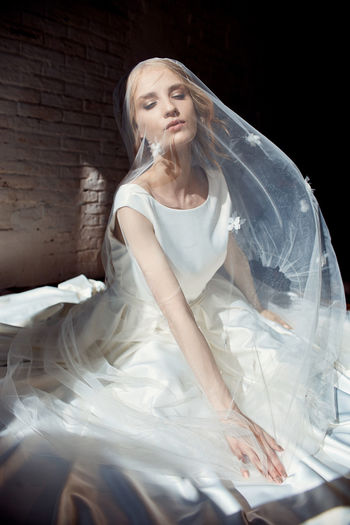 Bride wearing veil sitting on bed at home