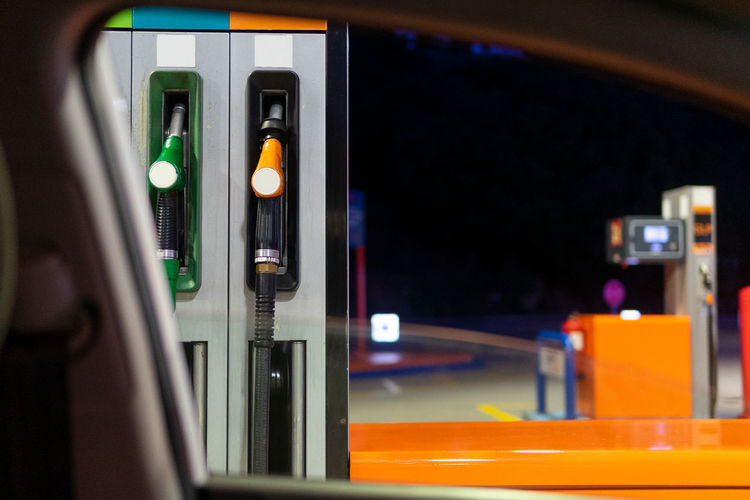 Through window of modern car of gasoline pumps with nozzles at filling station against dark night sky