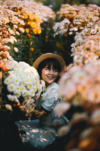 Smiling young woman crouching amidst flowering plants on field