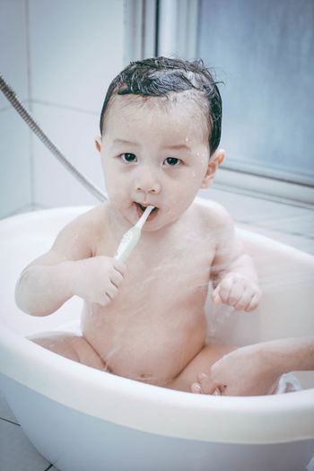 Portrait of cute baby boy brushing teeth in bathtub