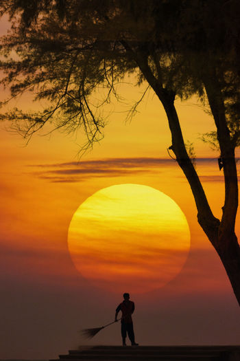 Silhouette man by tree against orange sky