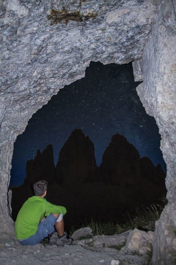 Man sitting in cave looking at starry sky