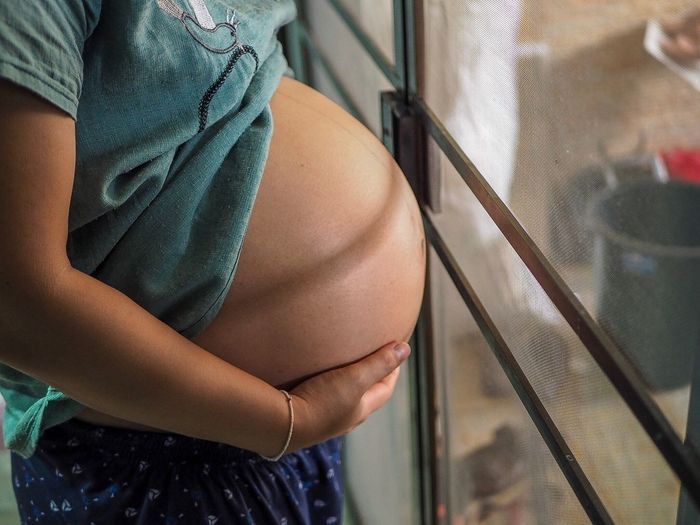 Midsection of pregnant woman standing by window