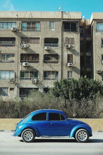 Car on road by buildings against blue sky