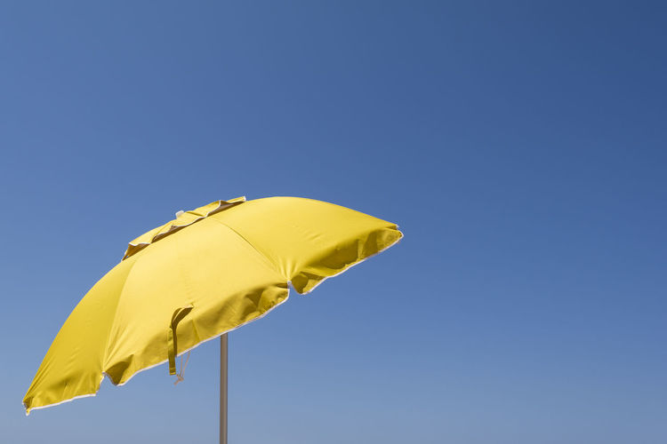 Low angle view of yellow umbrella against clear blue sky