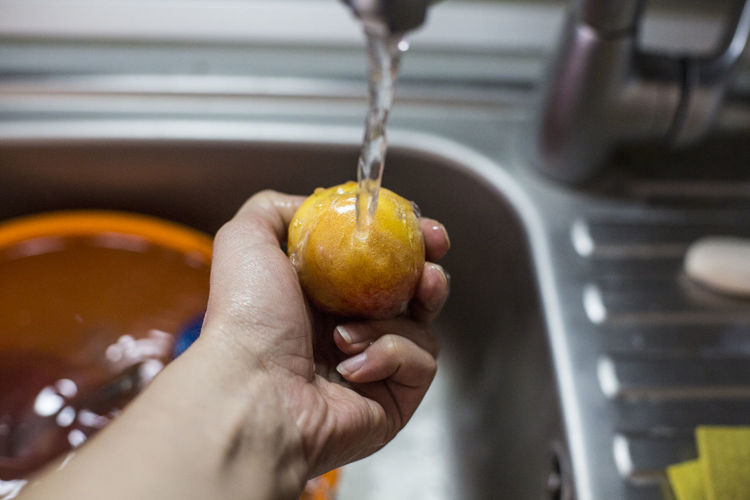 Cropped hand cleaning peach in kitchen