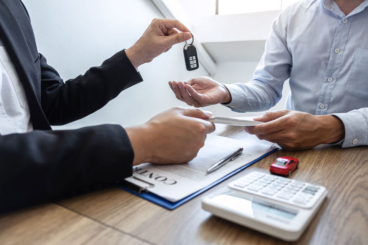 Agent giving car key to customer by papers and currency on table