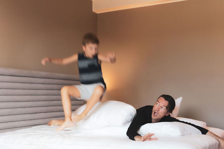 Playful kid in blurred motion jumping on a bed while playing with his father at home.