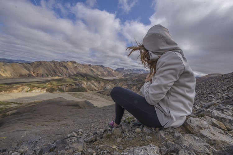 Woman sitting on top of mountain in the wind, in landmannalaugar