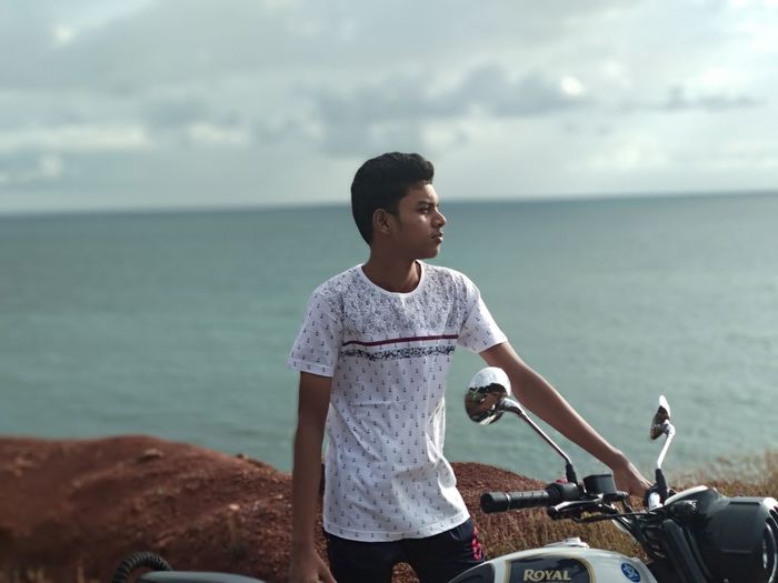 Young man standing at beach with motor cycle against sky