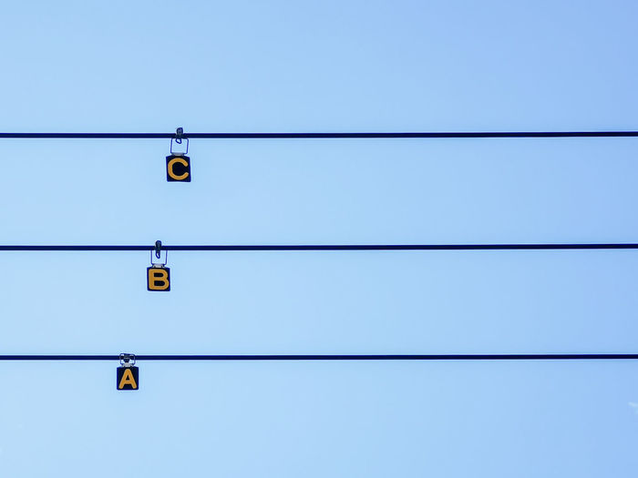Low angle view of alphabets hanging on cables against clear sky