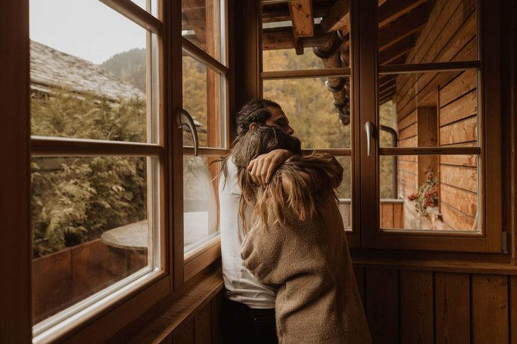Side view of man embracing anonymous girlfriend while spending time together in wooden cabin in daylight