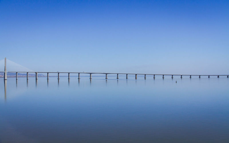 Bridge over calm sea against clear sky