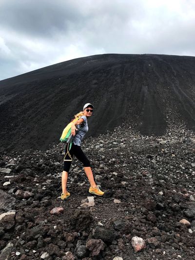 Side view of woman climbing mountain against sky