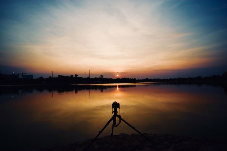 Tripod at beach against sky during sunset