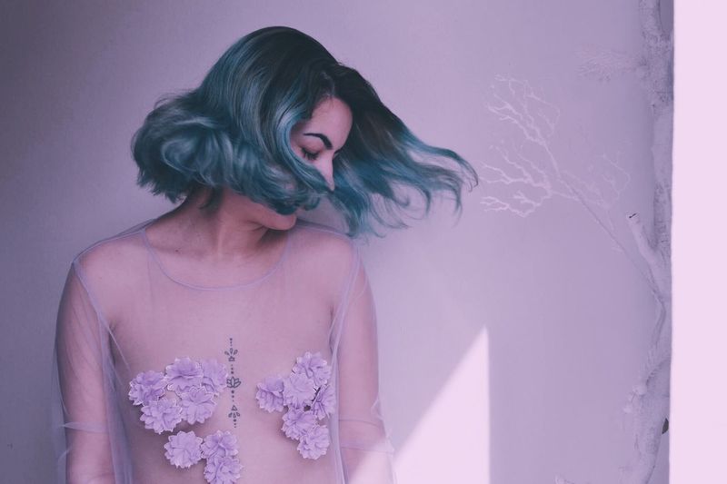 Sensuous woman wearing transparent while tossing dyed hair against white wall