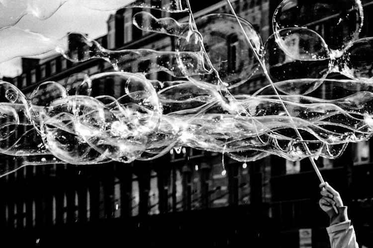 Cropped hand of person making bubbles against building
