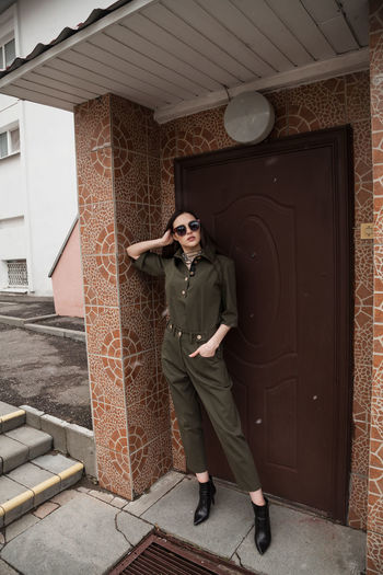 Full length front view portrait of tall slim brunette in green suit in urban setting, fashion  