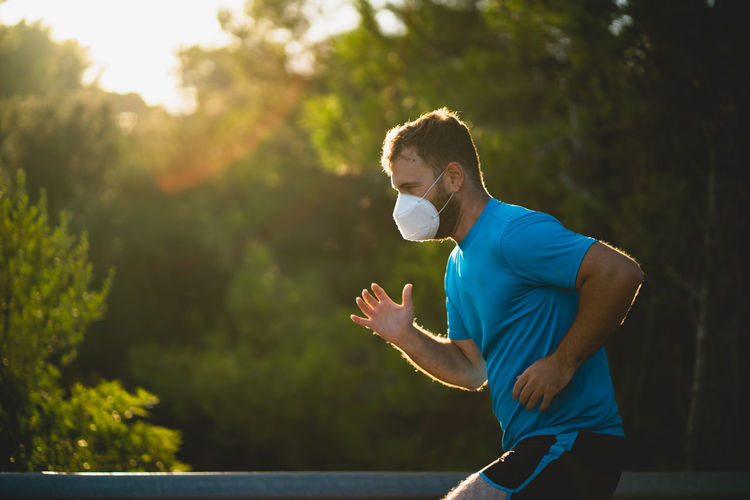 Side view of man wearing mask running against trees